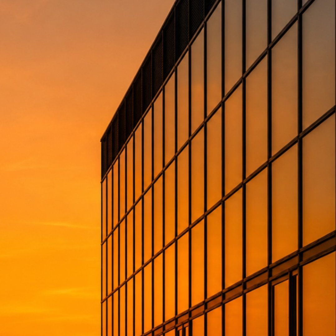 Modern building glass facade reflecting a warm orange sunset sky.