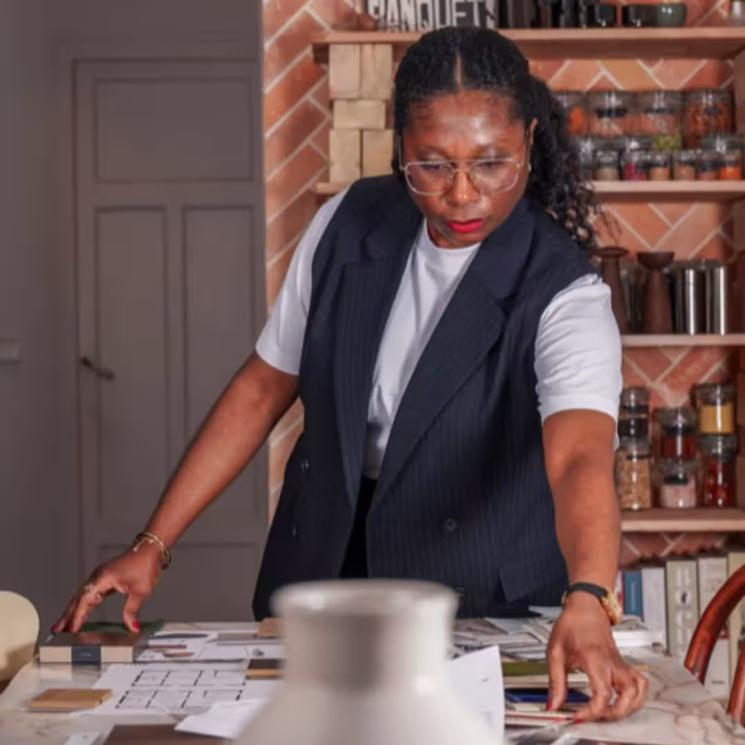 Woman wearing glasses arranging papers and materials on a table in a kitchen or workspace.
