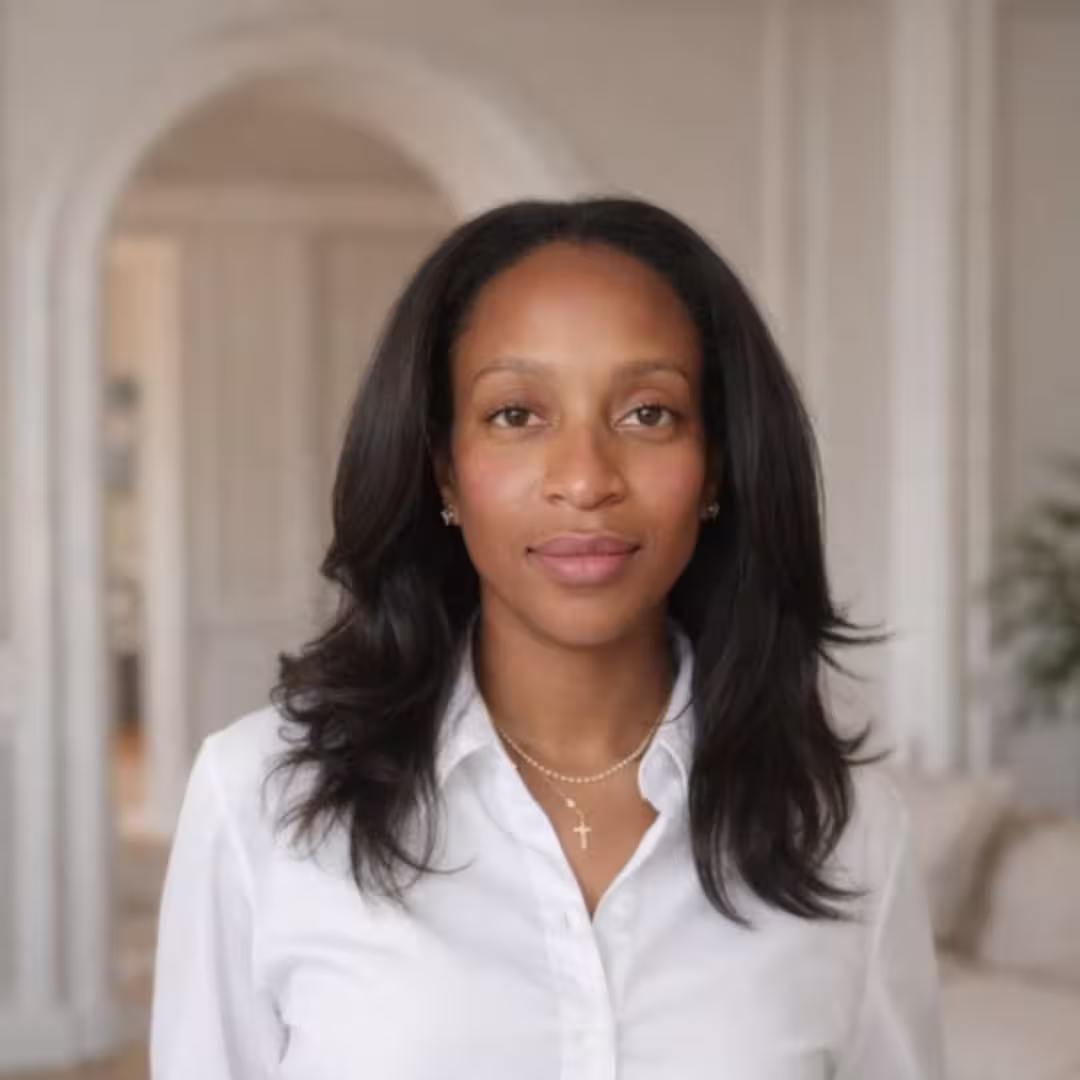 Woman with long dark hair wearing a white shirt and gold cross necklace, standing indoors.