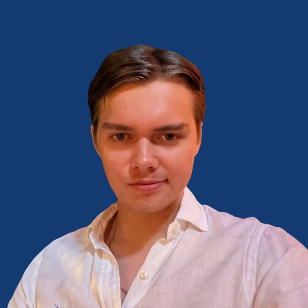 Young man with dark hair wearing a white shirt against a solid blue background.
