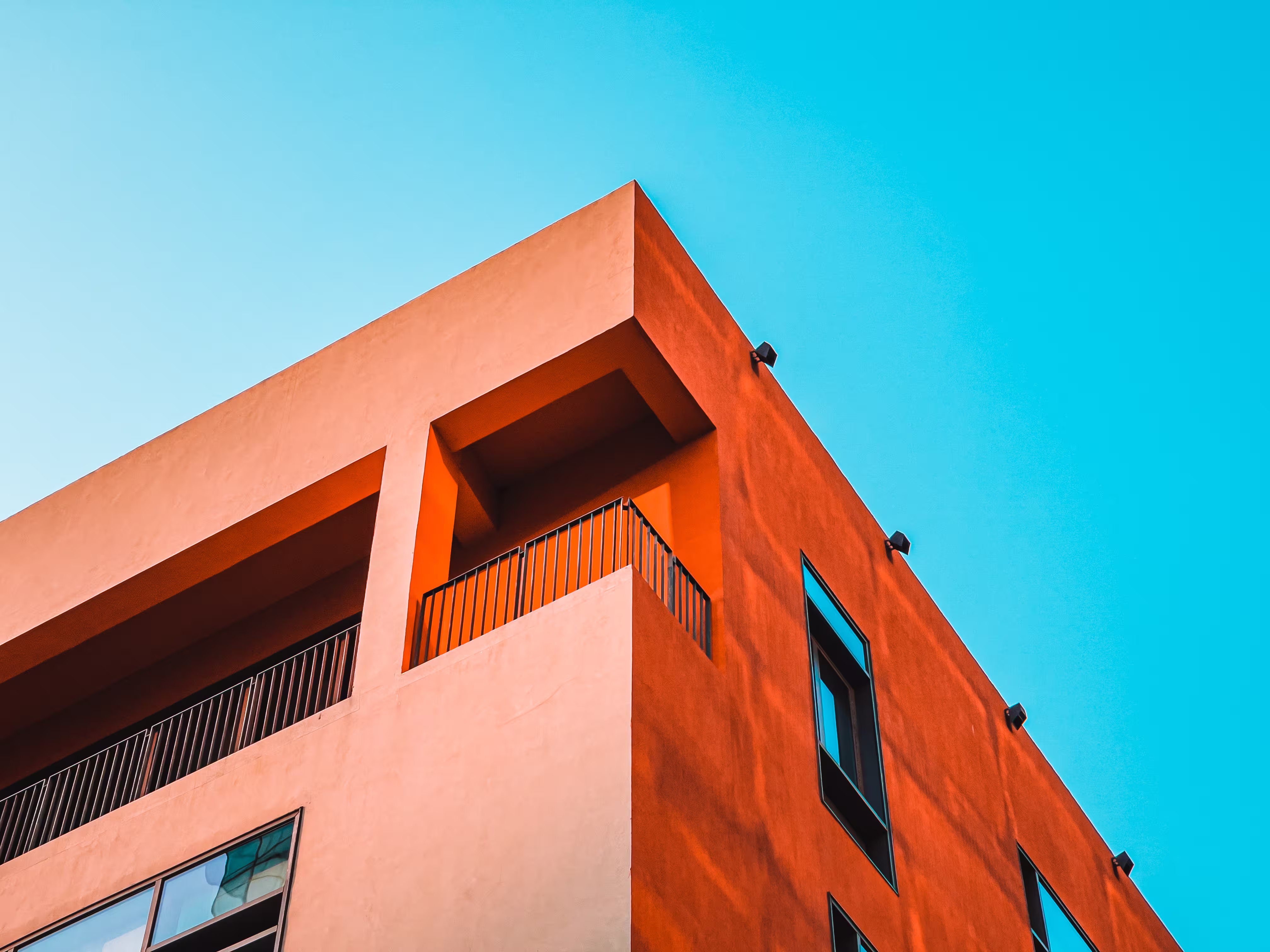 Low-angle view of a modern orange building facade with windows and balconies under a clear blue sky.
