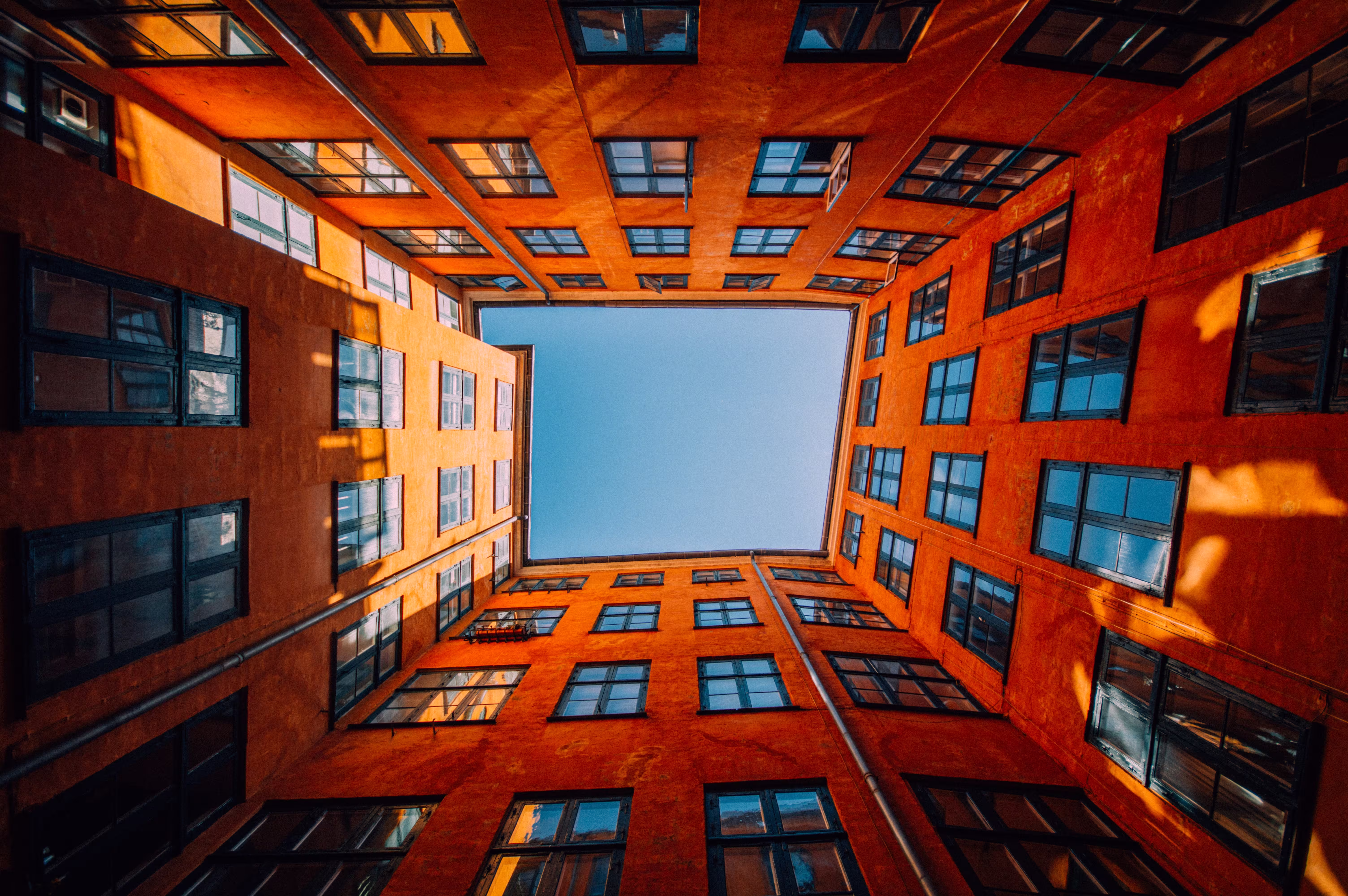Low-angle view of an orange high-rise building courtyard with blue sky visible at the top center.
