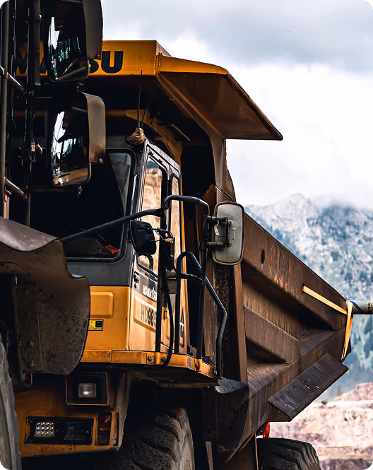Close-up of a yellow mining dump truck with mountains and cloudy sky in the background.