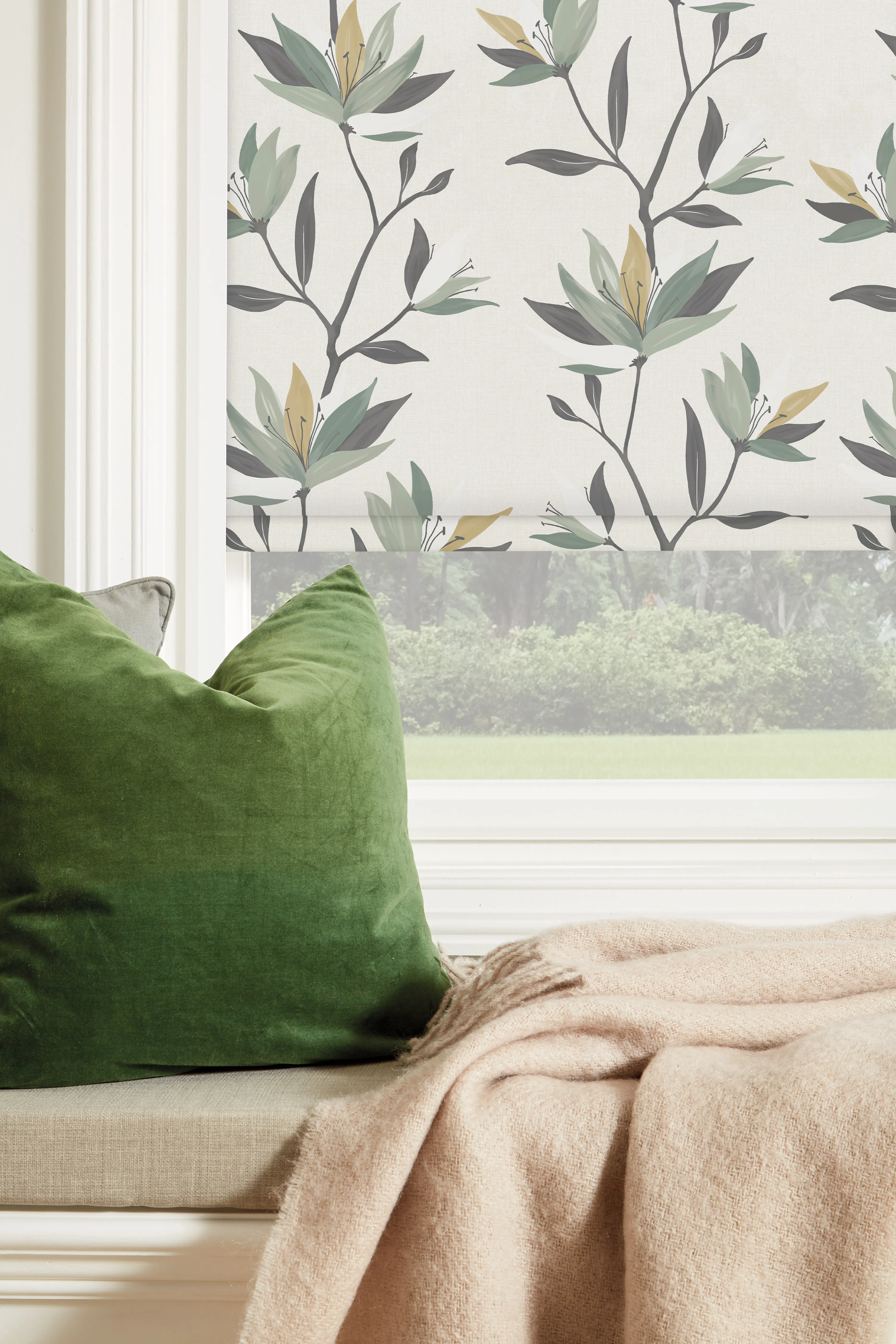 Window seat with green velvet pillow, beige cushion, beige blanket, and floral-patterned roller shade.