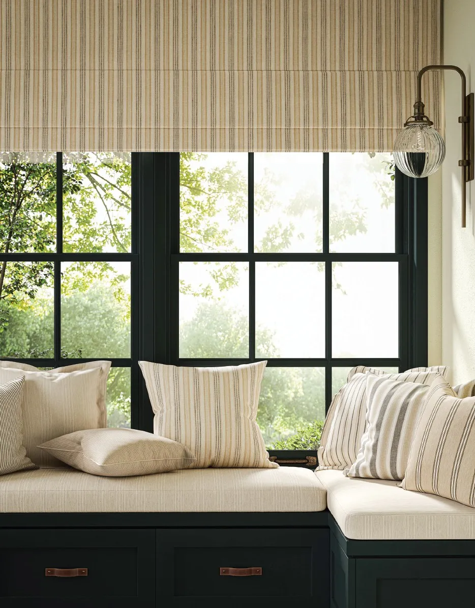 Cozy window seat with striped beige cushions and pillows under large paneled windows with a glass wall lamp.