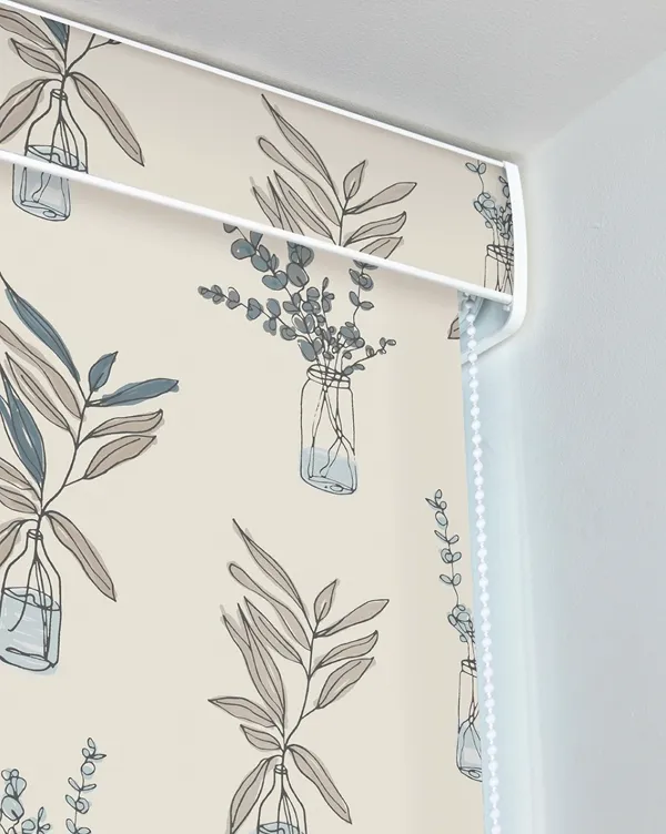 Beige roller blind with blue and gray leafy plant designs in glass jars, mounted on white wall.