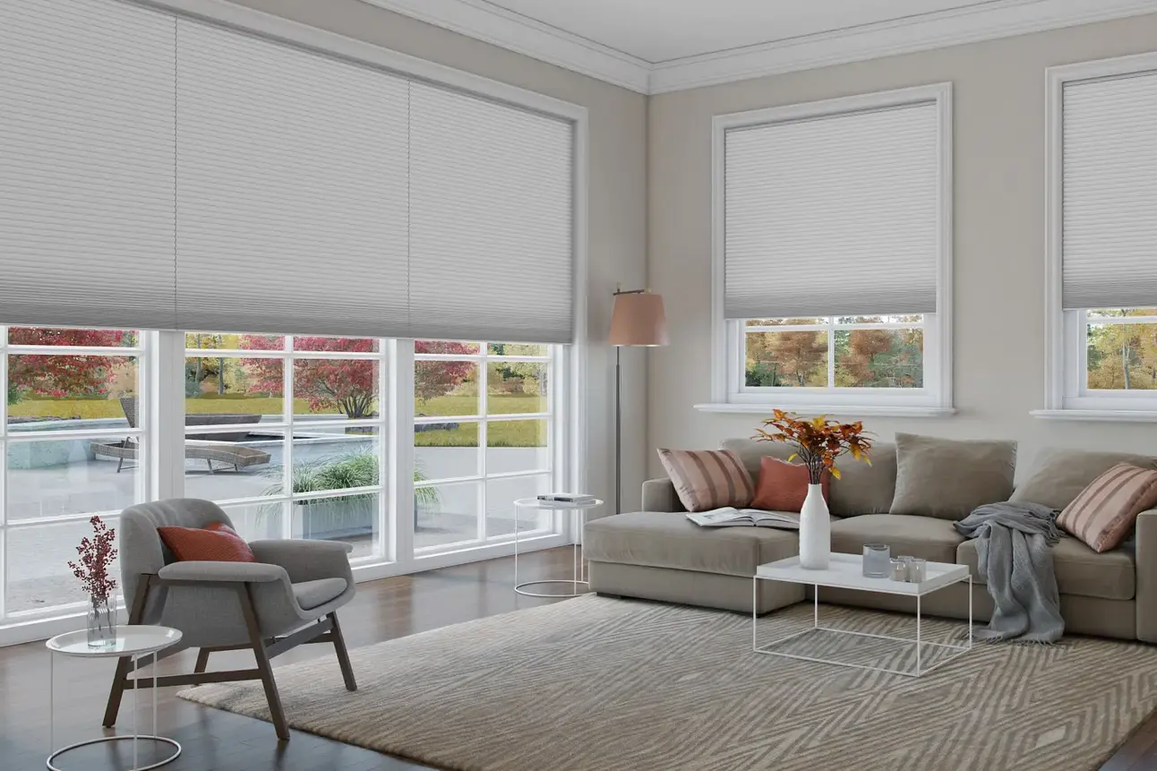 Modern living room with gray cellular shades on windows, beige sofa, chair, and white tables.