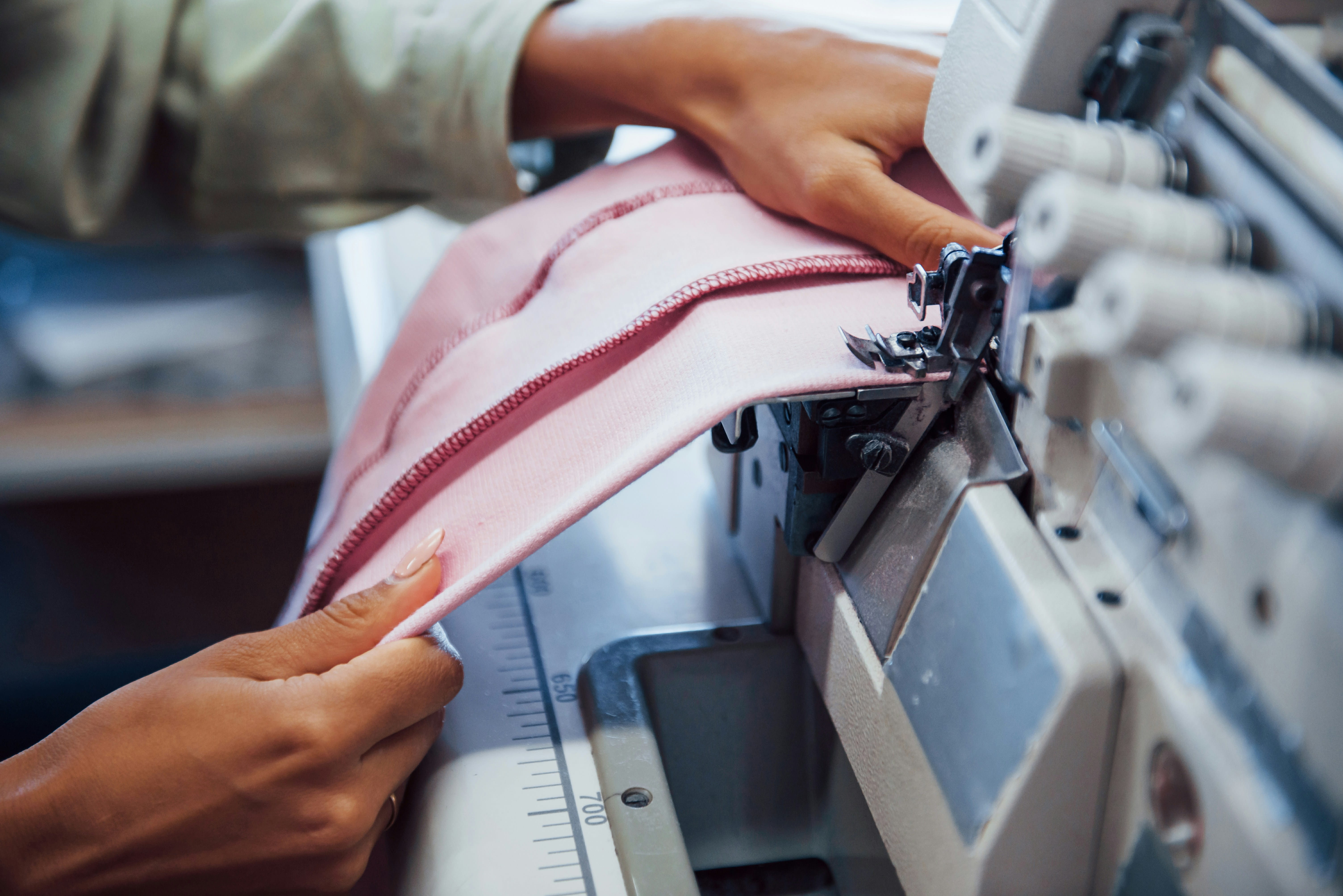 Hands guiding pink fabric through an industrial sewing machine for stitching.