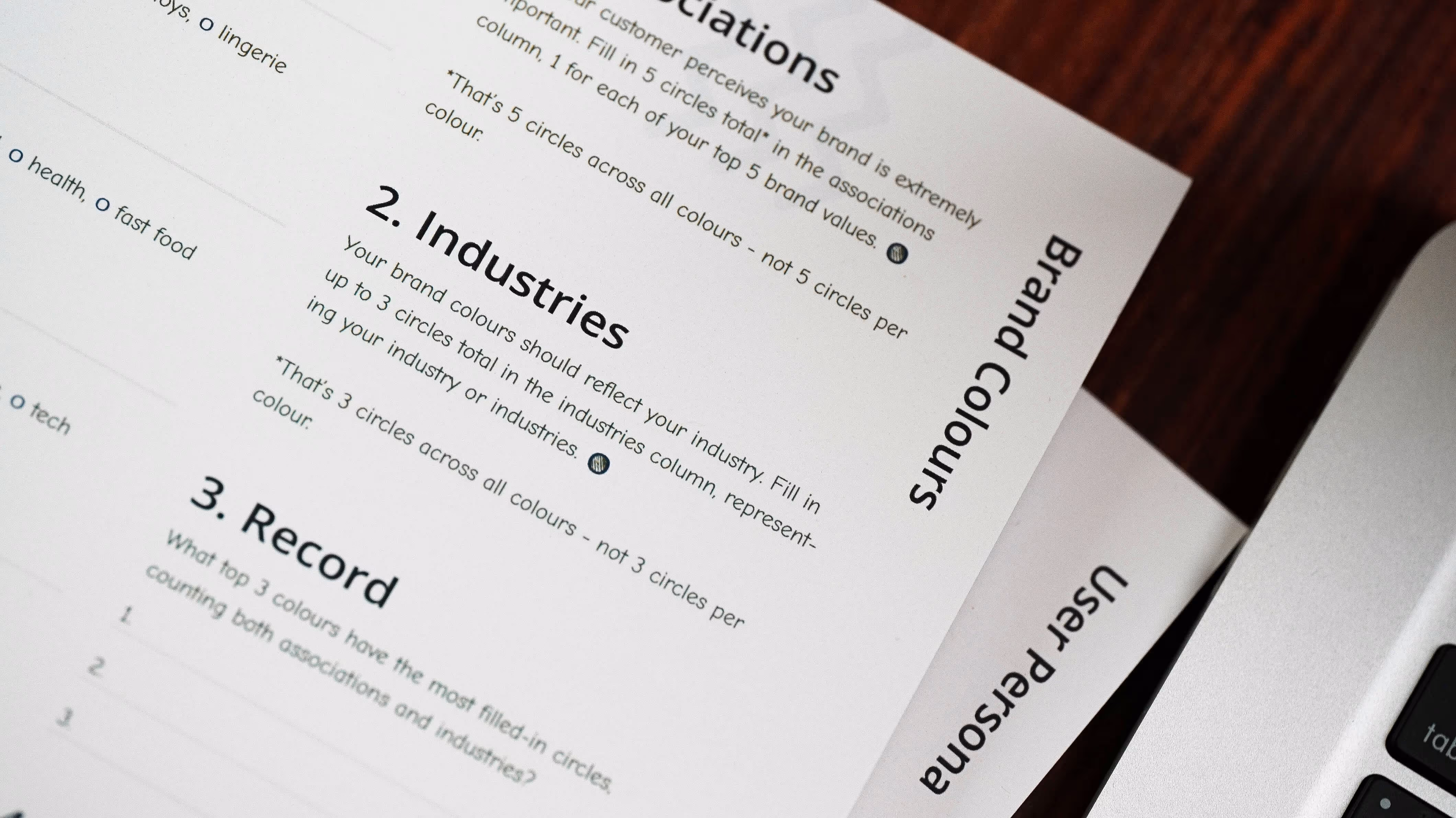 Close-up of a printed worksheet about brand colours and industries, next to a laptop keyboard.