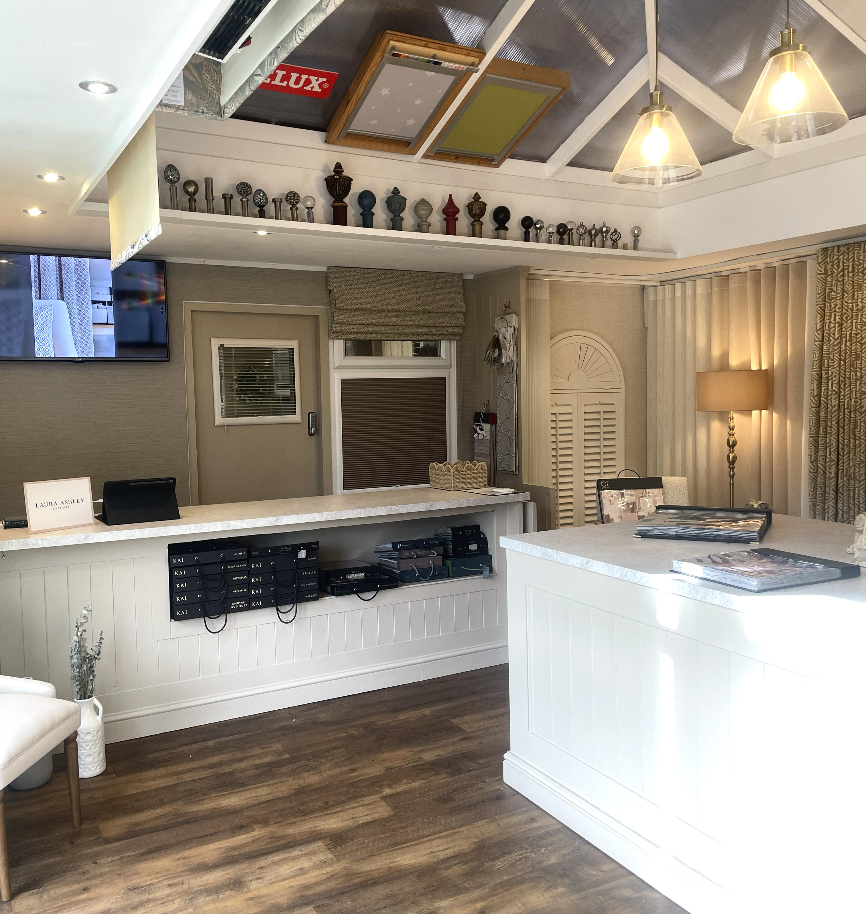 Bright modern showroom with white counters, wood floor, samples on counters, and decorative curtain rods displayed.