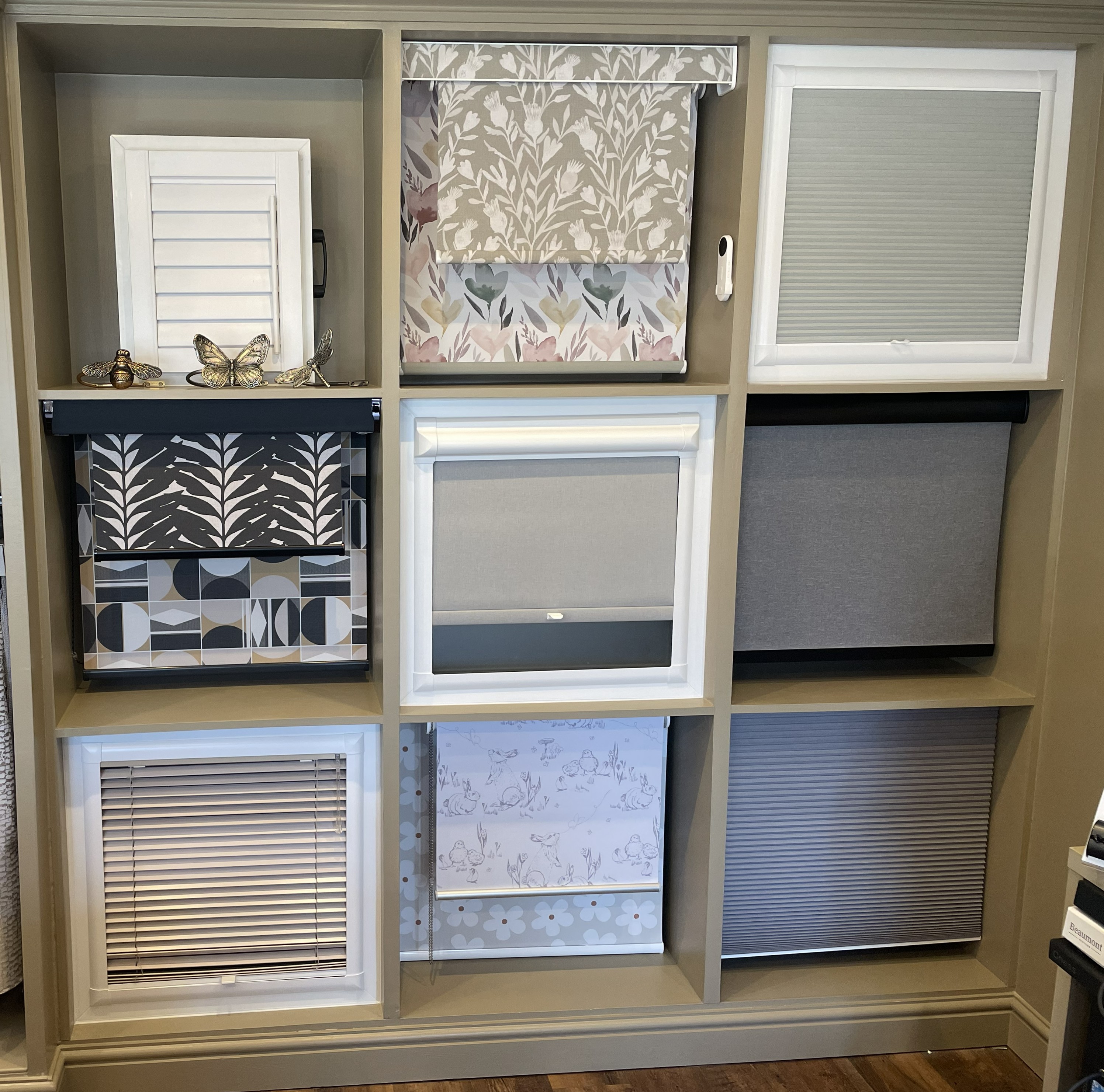 Wall display of nine window blinds and shutters in various patterns and shades.