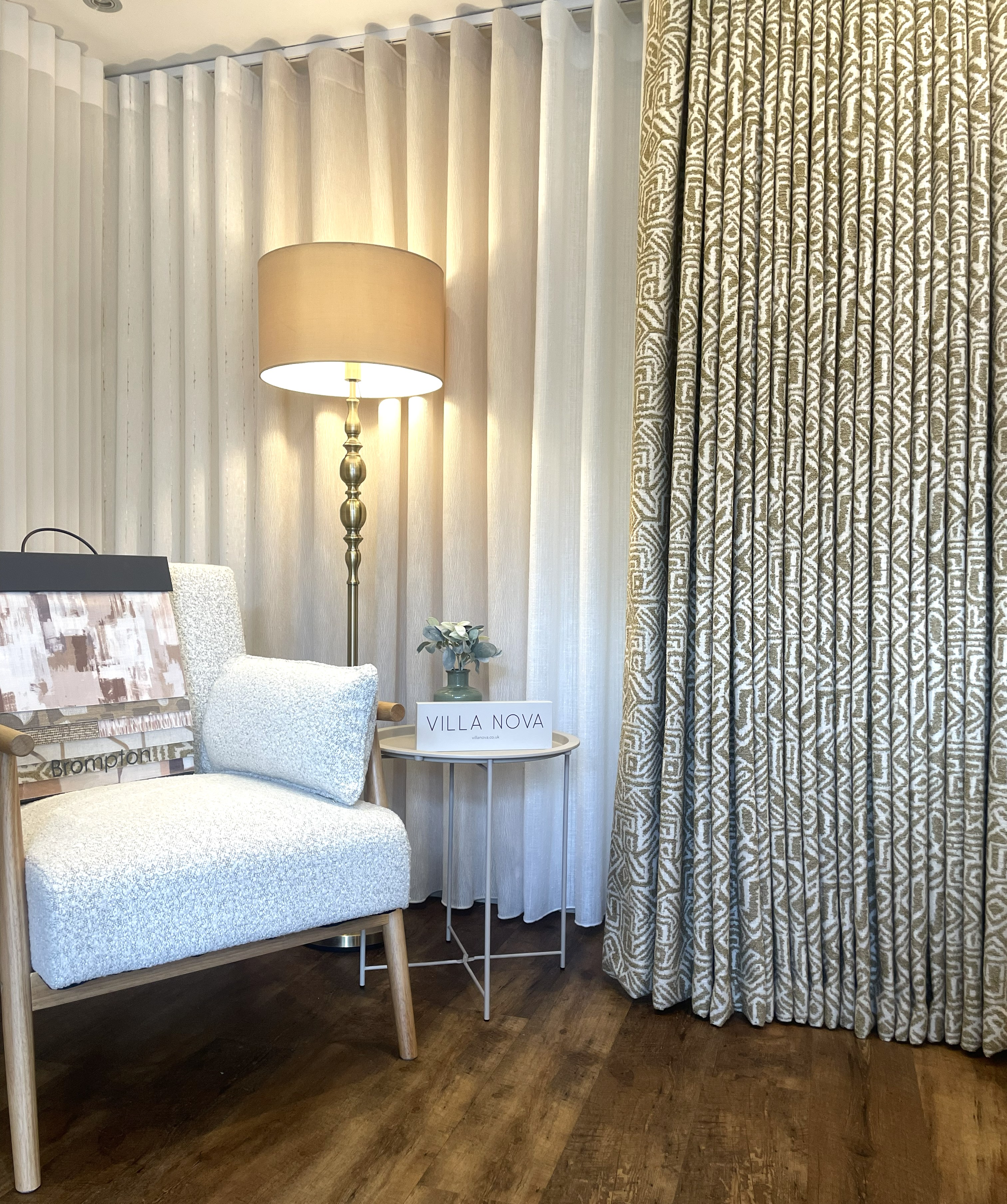 Cozy corner with a white cushioned chair, a floor lamp, a small round table, and patterned curtains.