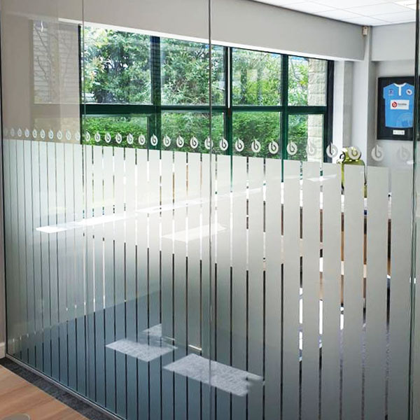 Office interior with a glass wall featuring vertical frosted stripes and a view of greenery outside.
