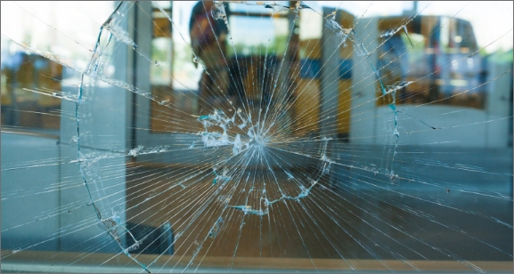 Close-up of a circular shattered glass pane with cracks radiating from the impact point.