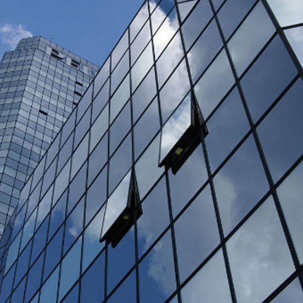 Glass facade of office buildings reflecting blue sky and clouds with two open windows.