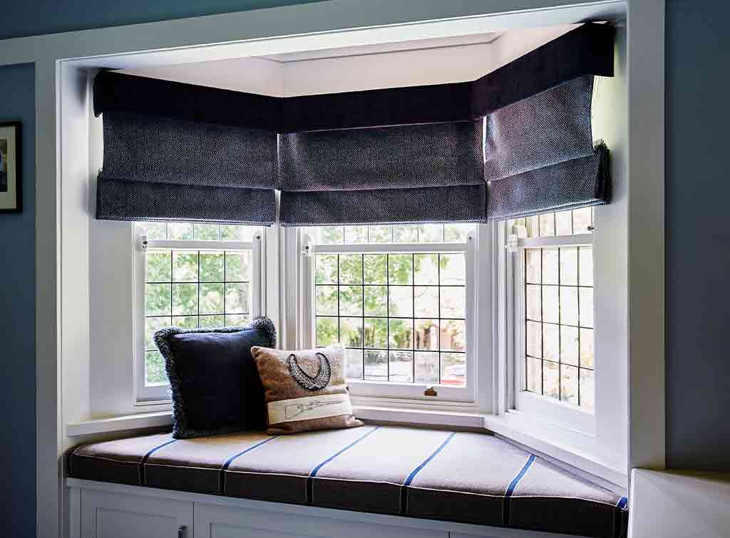 Cozy bay window seating with two decorative pillows and lowered dark roman shades.
