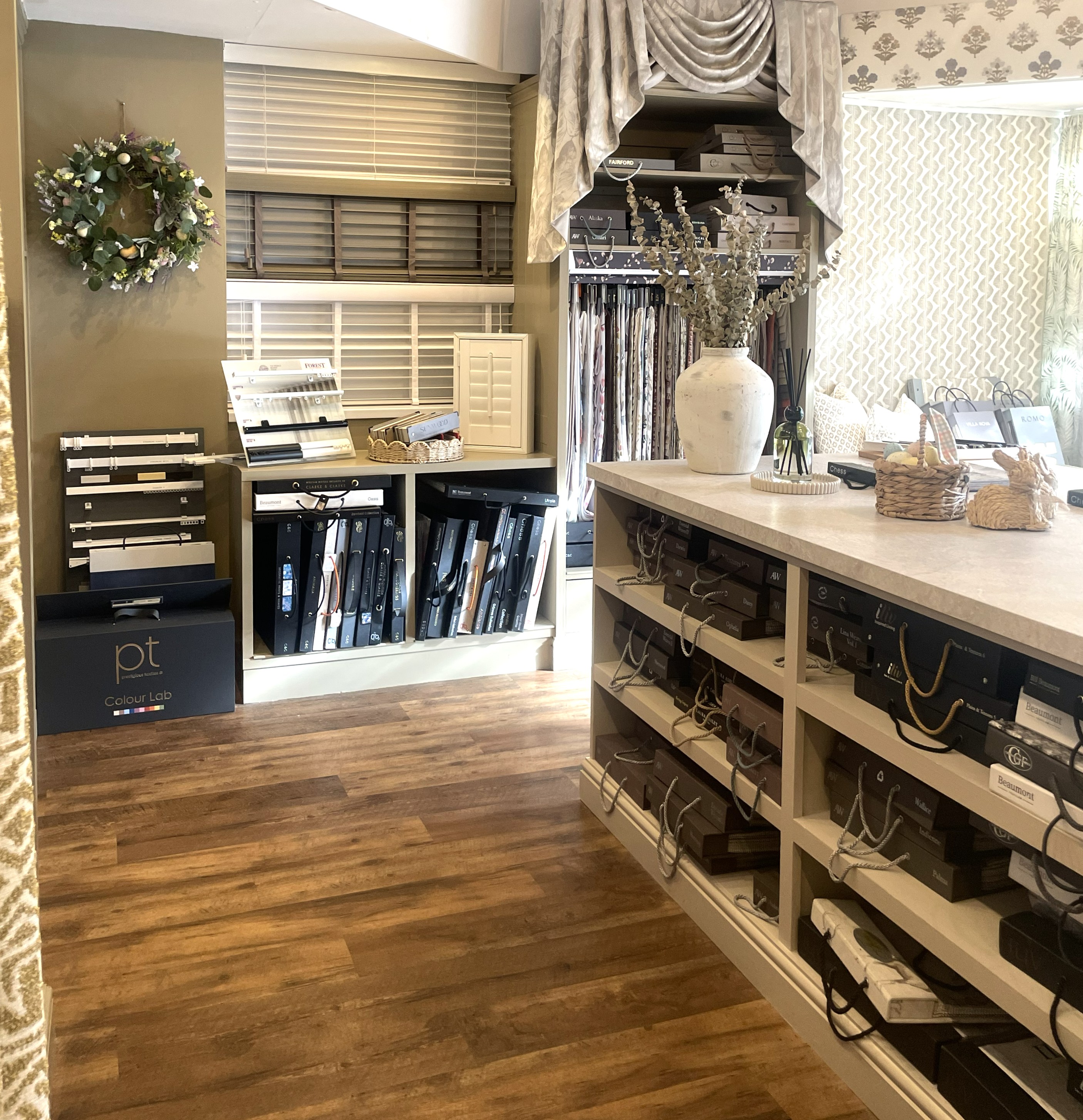Interior of a fabric and blinds showroom with shelves of samples and decorative plants on a counter.