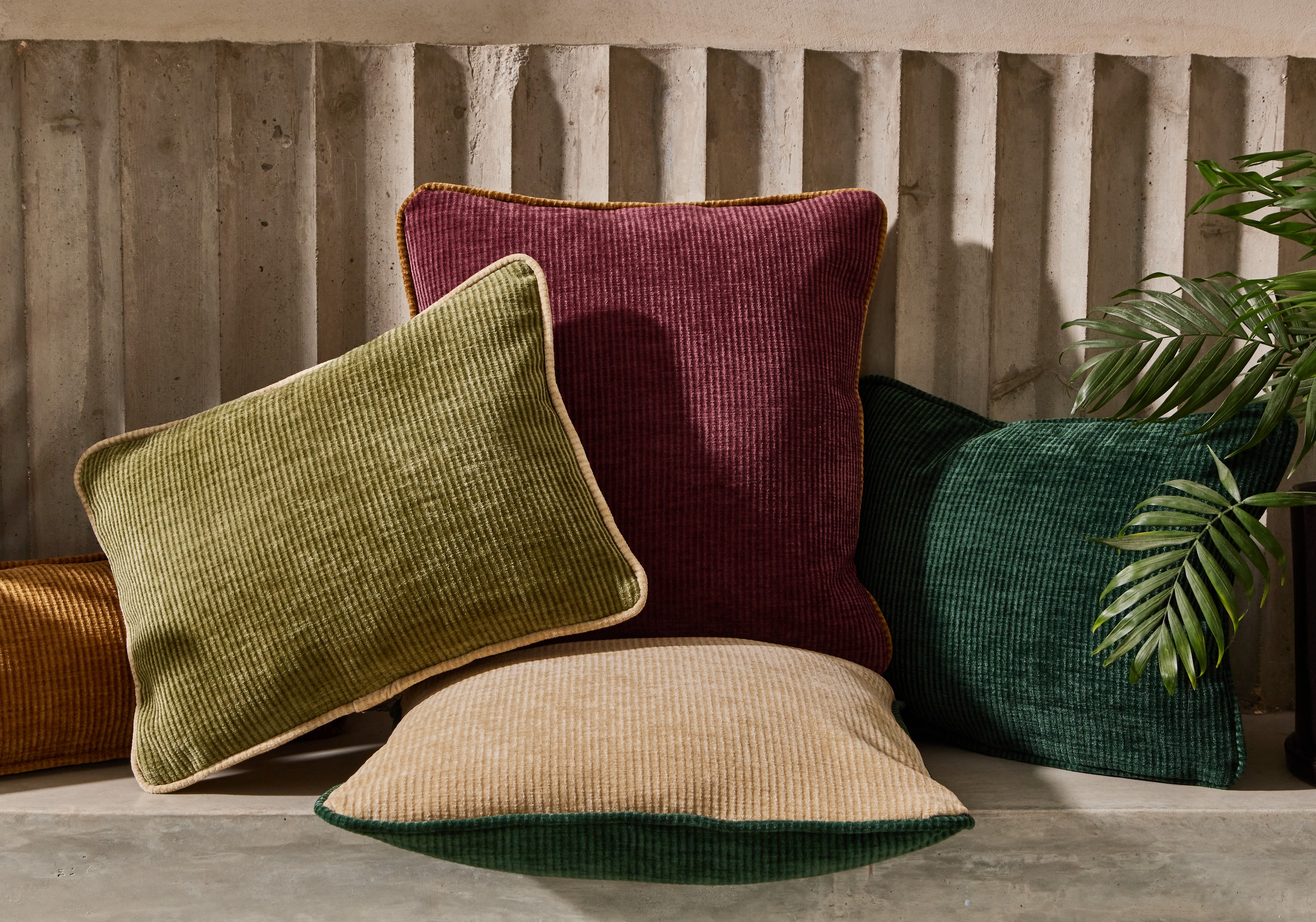 Three patterned pillows on a bench next to fabric sample books labeled Villa Nova and Romo.