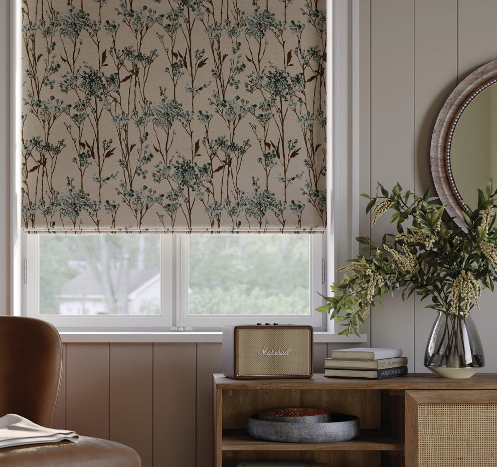 Window with floral-patterned roller shade, green velvet pillow, beige cushion, and soft beige throw.