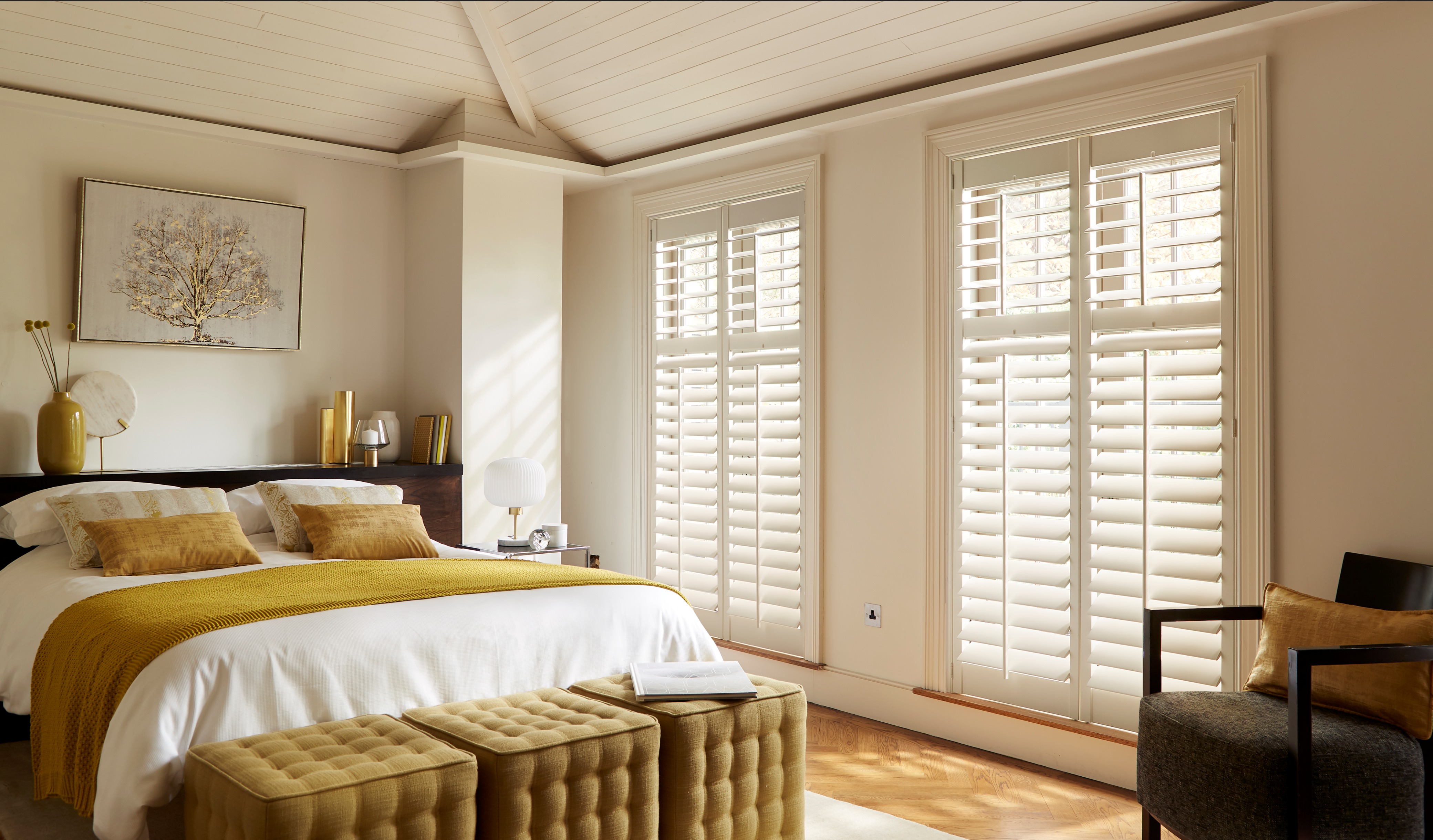 Bedroom with white plantation shutters on windows, white bed with mustard yellow accents, and modern decor.