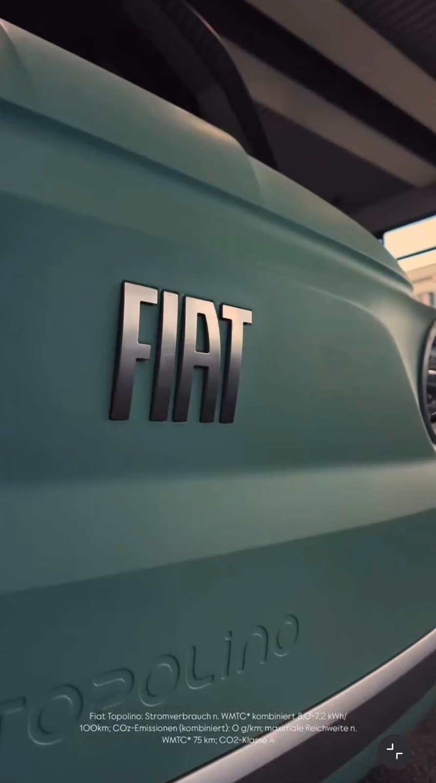 Nahaufnahme des FIAT-Schriftzugs auf der hellgrünen Karosserie eines Fiat Topolino, mit teilweise sichtbarem Scheinwerfer und Dachstruktur im Hintergrund.