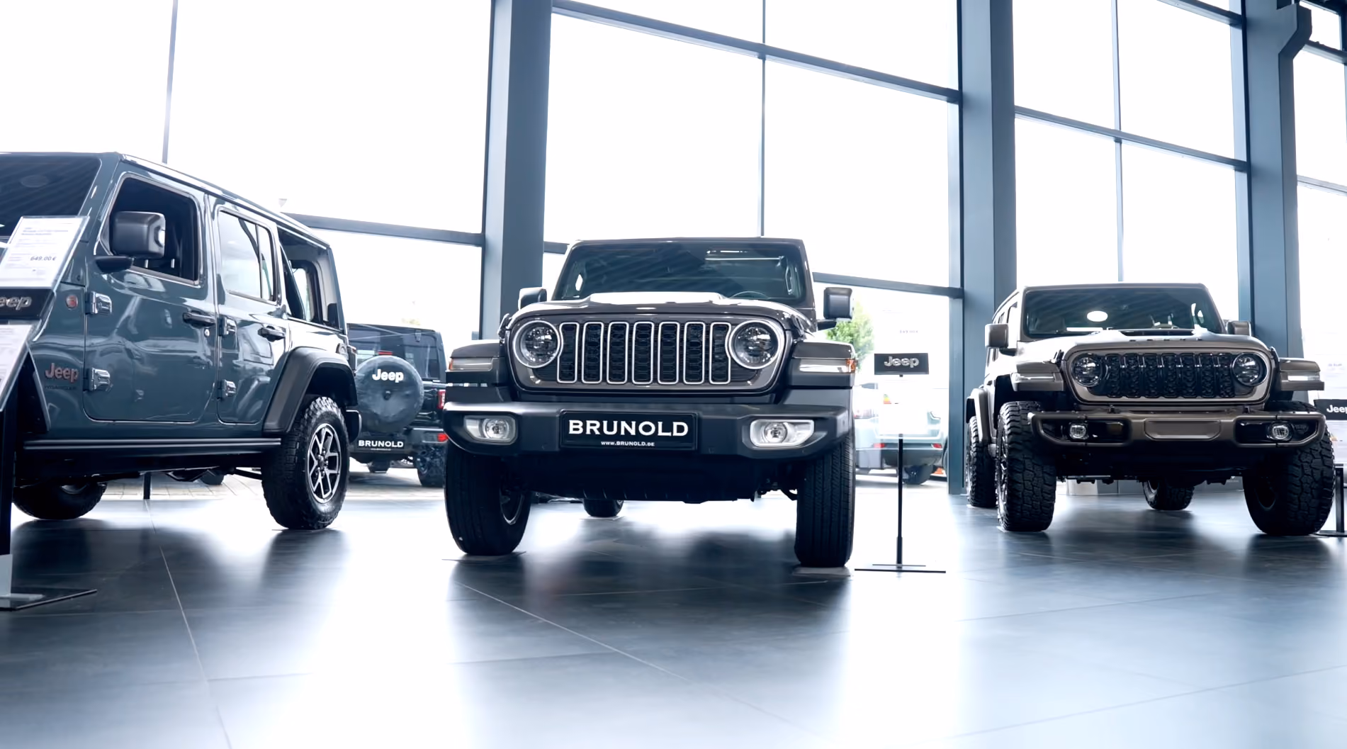 Frontansicht von drei Jeep-Geländewagen in einem hellen Autohaus mit großen Fenstern, mittleres Fahrzeug zeigt ein Schild mit der Aufschrift BRUNOLD.