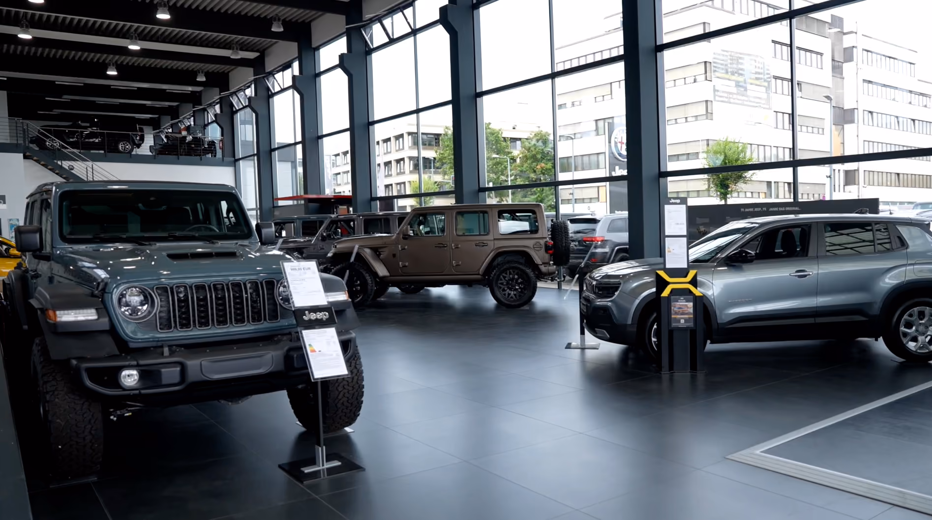 Innenansicht eines modernen Autohauses mit mehreren ausgestellten Jeep-Geländewagen, großen Glasfenstern, schwarzem Boden und Deckenbeleuchtung.