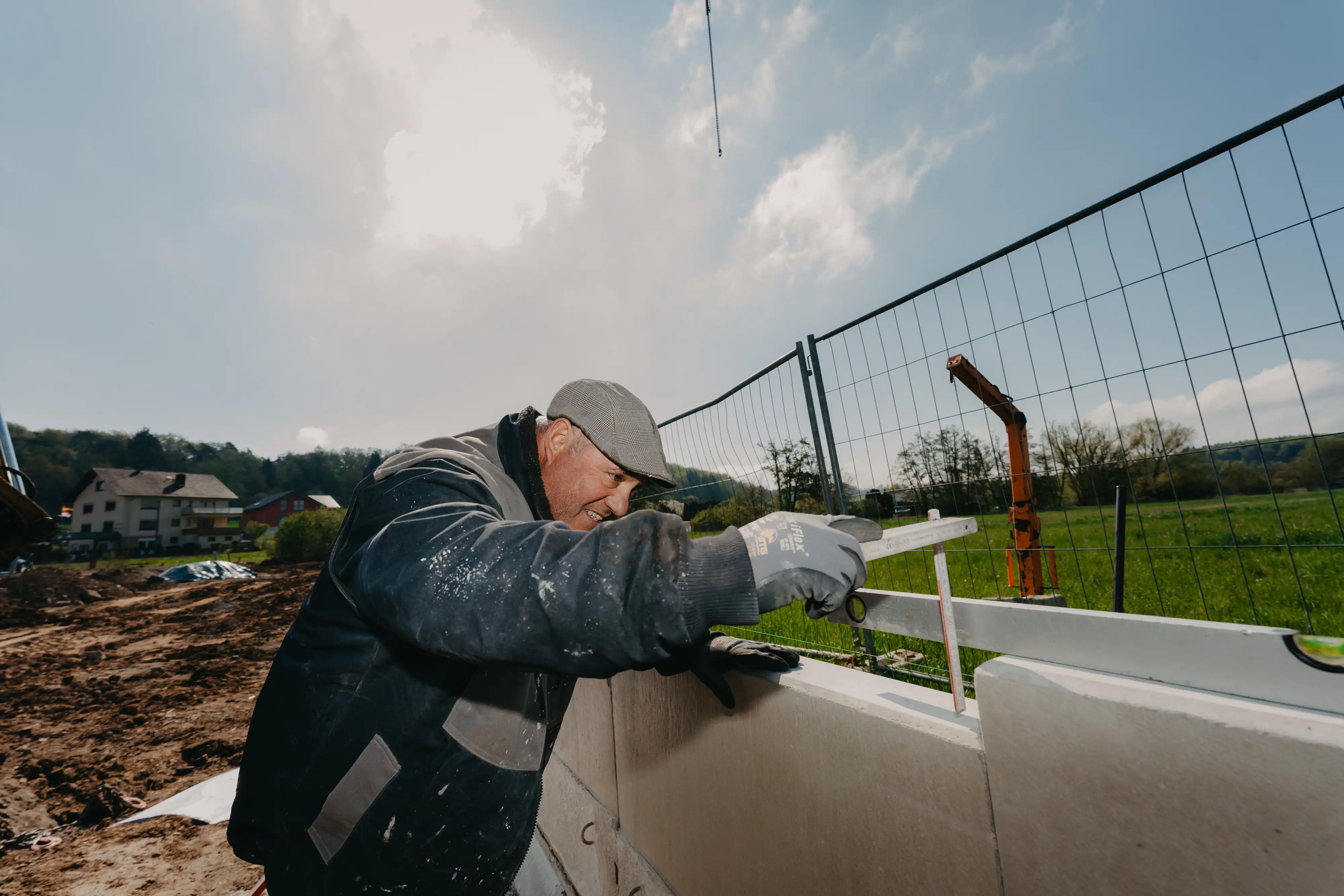 Bauarbeiter misst mit Wasserwaage auf einer Baustelle eine Wand bei sonnigem Wetter mit blauem Himmel.