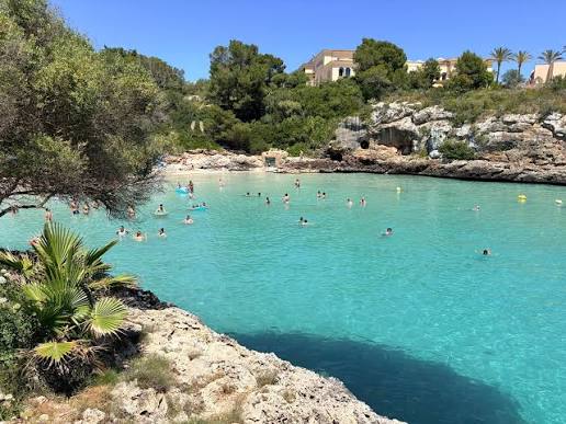 Sandy Cala Ferrera beach with clear water and resort buildings nearby