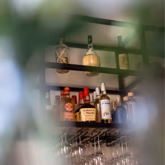 Shelves with various liquor bottles and hanging wine glasses in blurred view through glass.