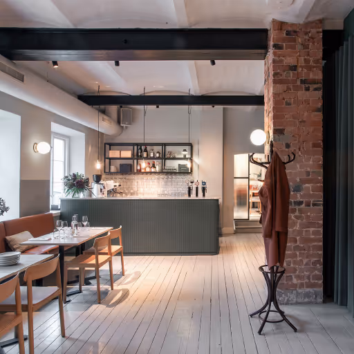Modernt kafé med trästolar, bord och baravdelning under svarta takbalkar.