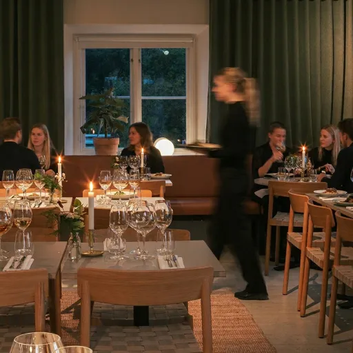 Människor äter middag i ett mysigt rum med levande ljus och en servitris som går förbi.