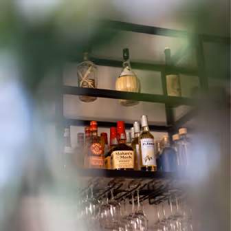 Hylla med olika spritflaskor och glas hängande under i en bar.