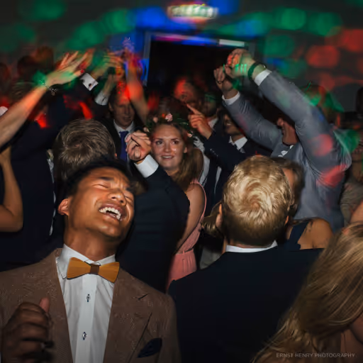 Människor i formella kläder dansar och firar under färgglada ljus på en fest.