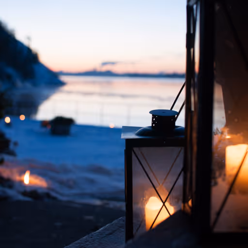 En tänd lykta vid en strand vid solnedgång med havet och klippor i bakgrunden.