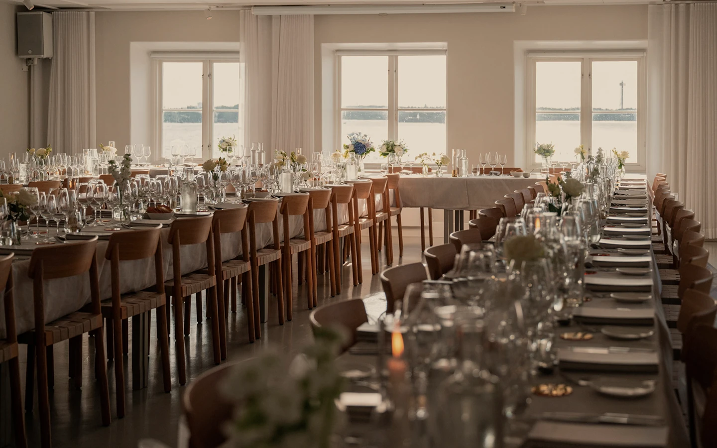 Vackert dukade bord med glas, blommor och porslin i ett rum med stora fönster ut mot havet.