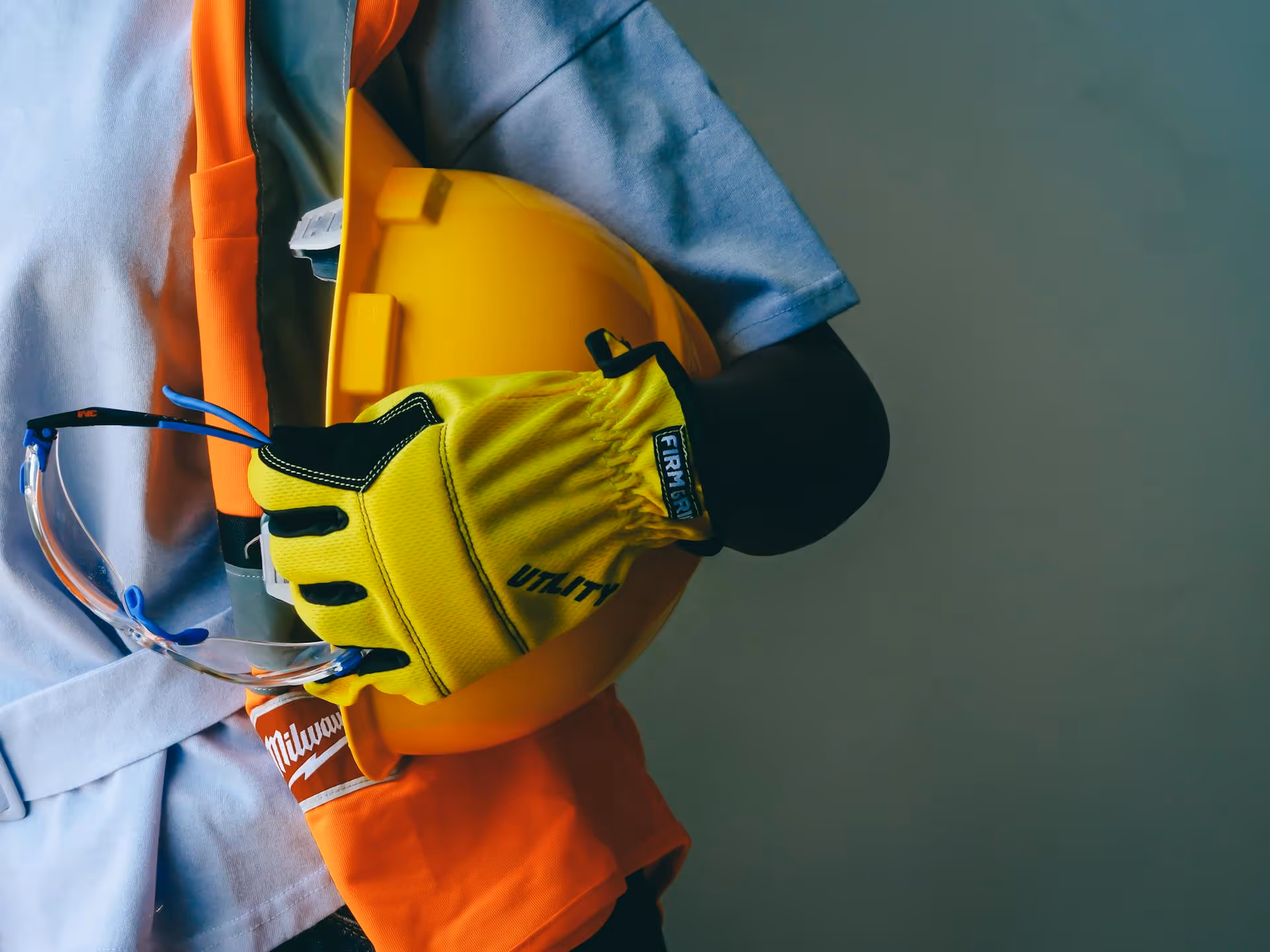 Person holding a yellow hard hat, yellow utility gloves, and safety glasses with workwear.