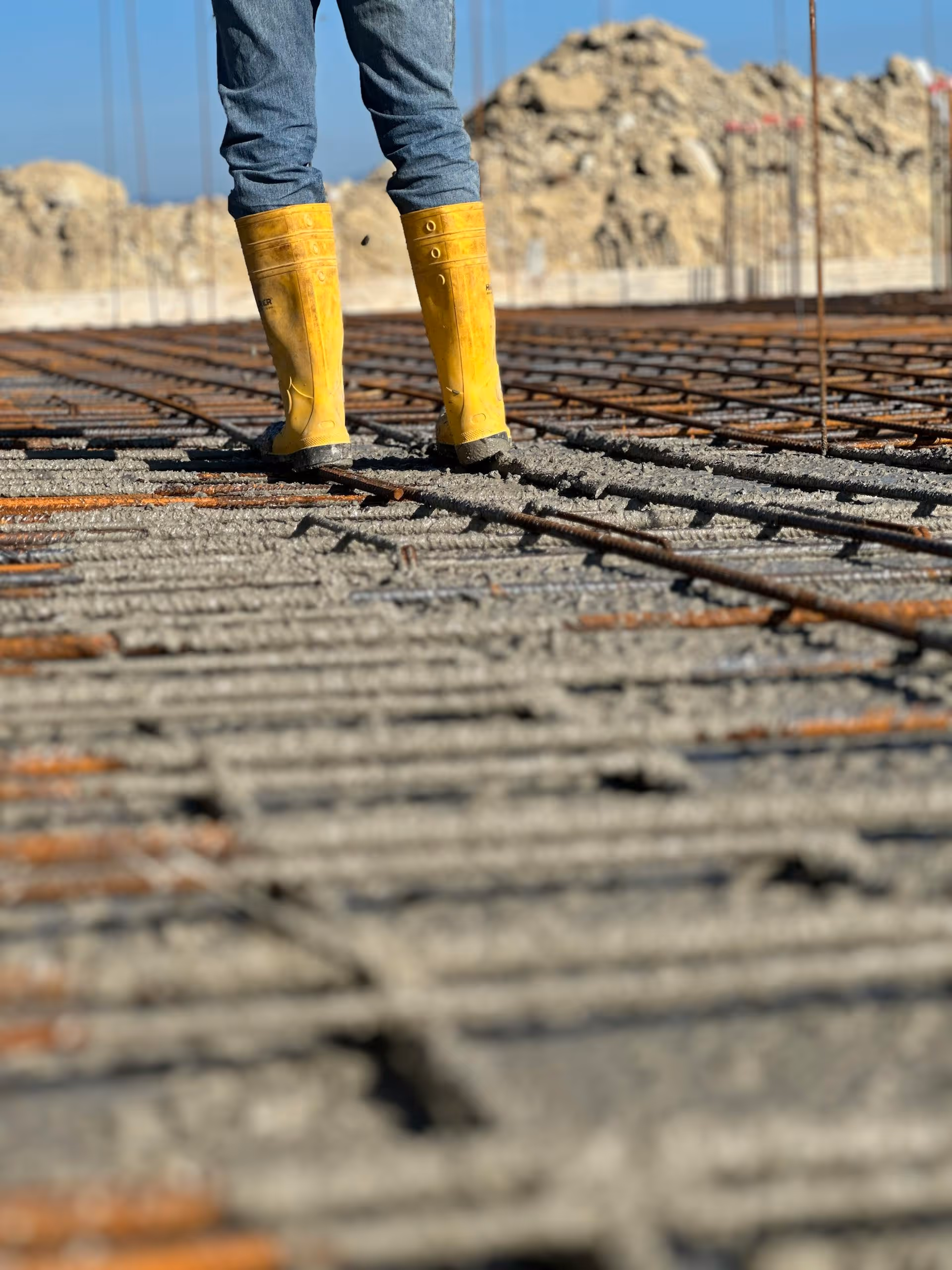 Person wearing yellow boots standing on wet concrete with metal rebar at a construction site.