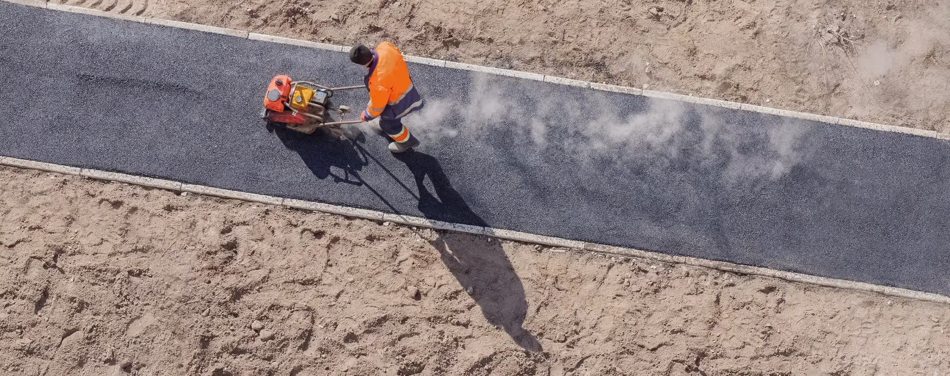 Worker using roller on tarmac