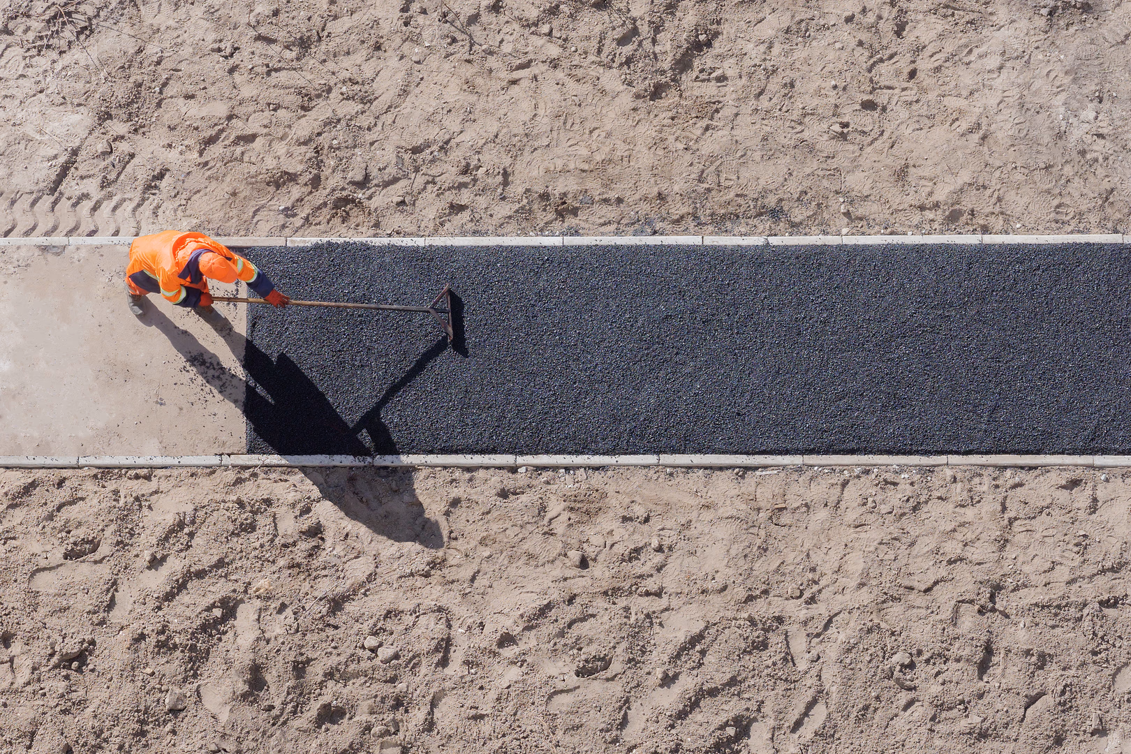 Worker using roller on tarmac