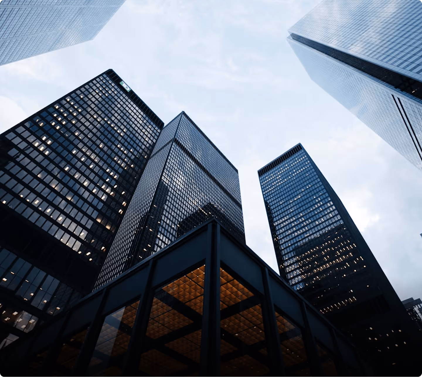 Low-angle view of tall glass office skyscrapers under a cloudy sky at dusk.