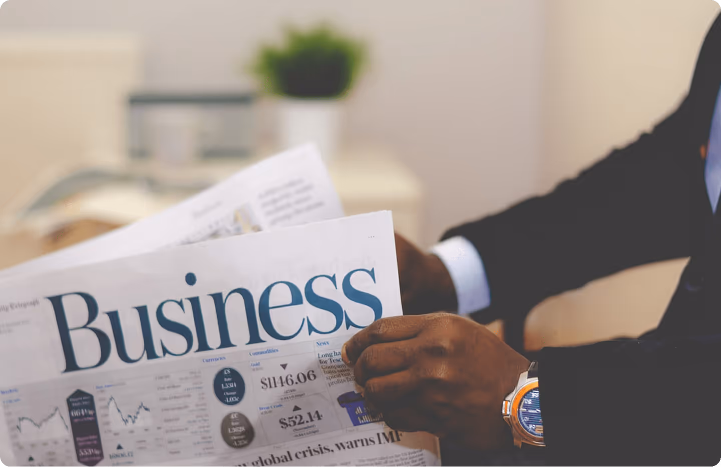 Person in suit reading a business newspaper showing stock market data and financial news.