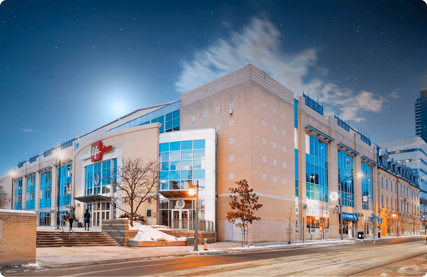 Modern building with large glass windows and snow on the ground at dusk under a clear starry sky.