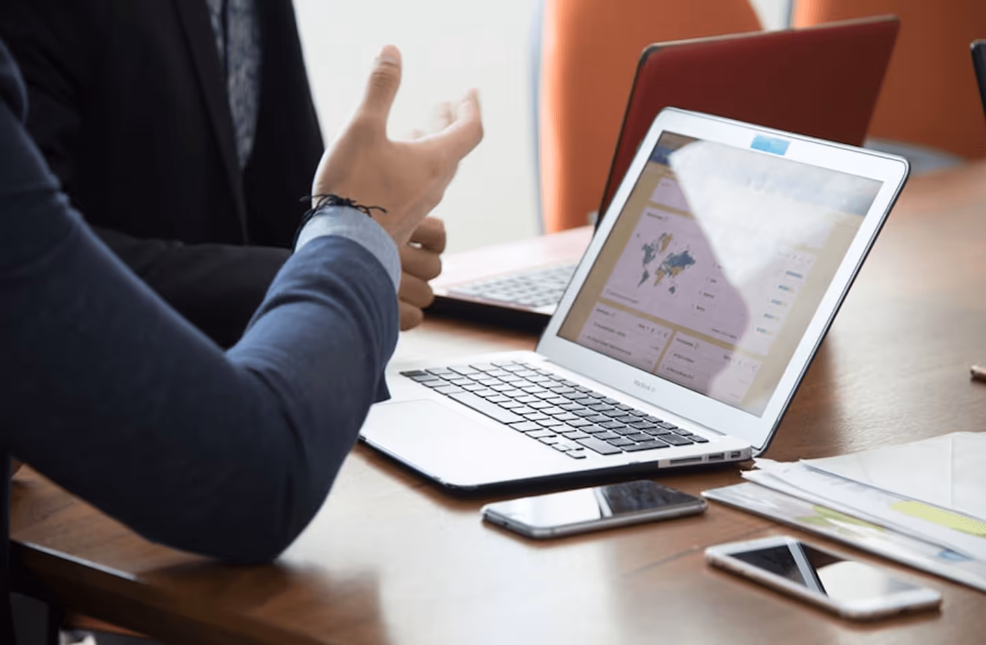 Two people in a discussion with a laptop showing a world map and smartphones on the table.