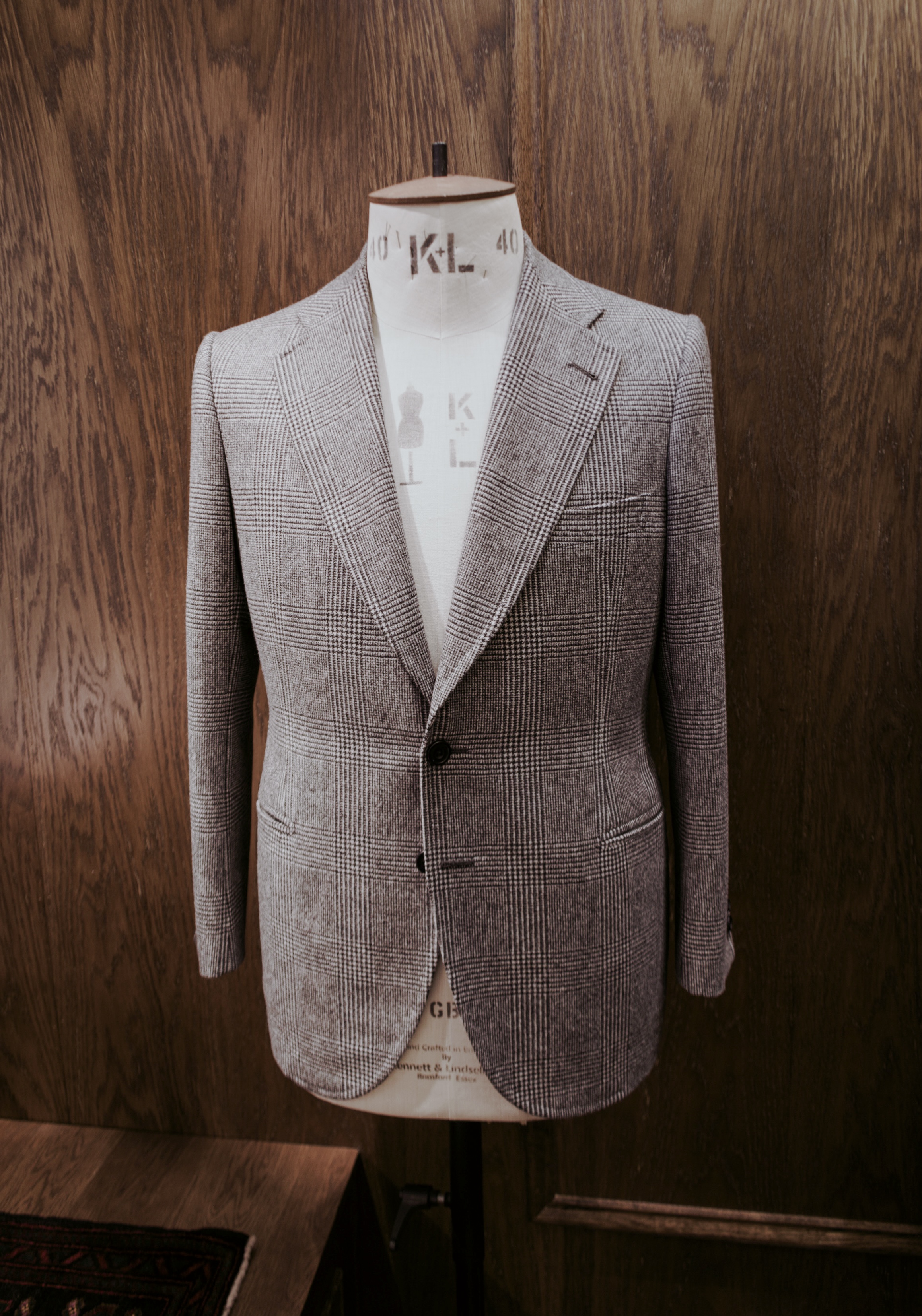 A grey Glen check Monte Lys bespoke jacket on a tailor’s form against warm oak panelling.