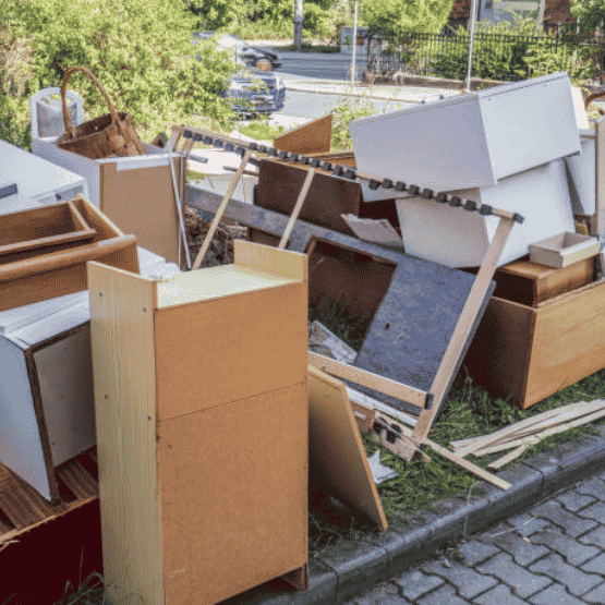 Pile of discarded furniture and wooden items on a grassy curb beside a street.