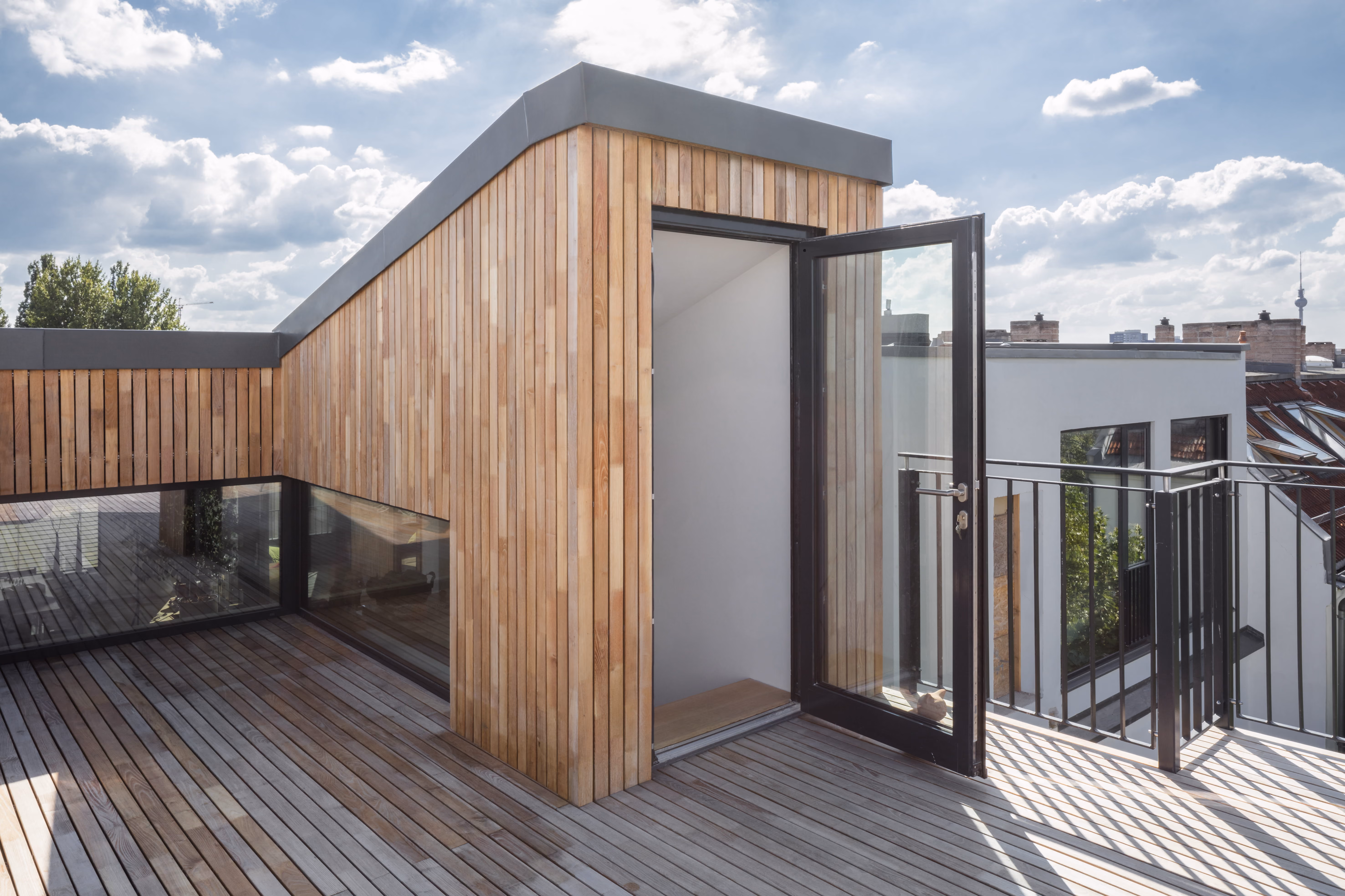 Holzverkleideter Aufbau auf der Dachterrasse des Penthouse mit Glastür und umlaufender Holzdielen-Terrasse