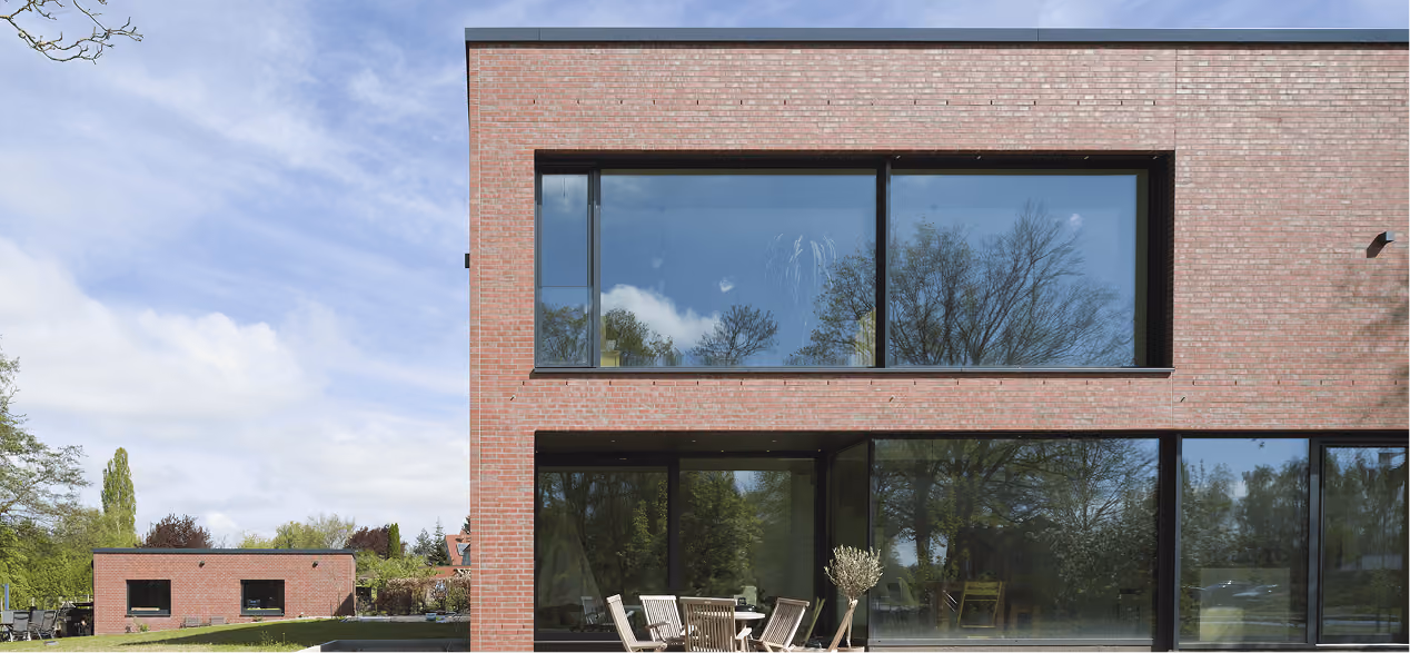 Backsteinfassade eines Wohnhauses mit großer Fensterfront und Terrassenmöbeln im Vordergrund, Beispielprojekt aus dem Referenzportfolio