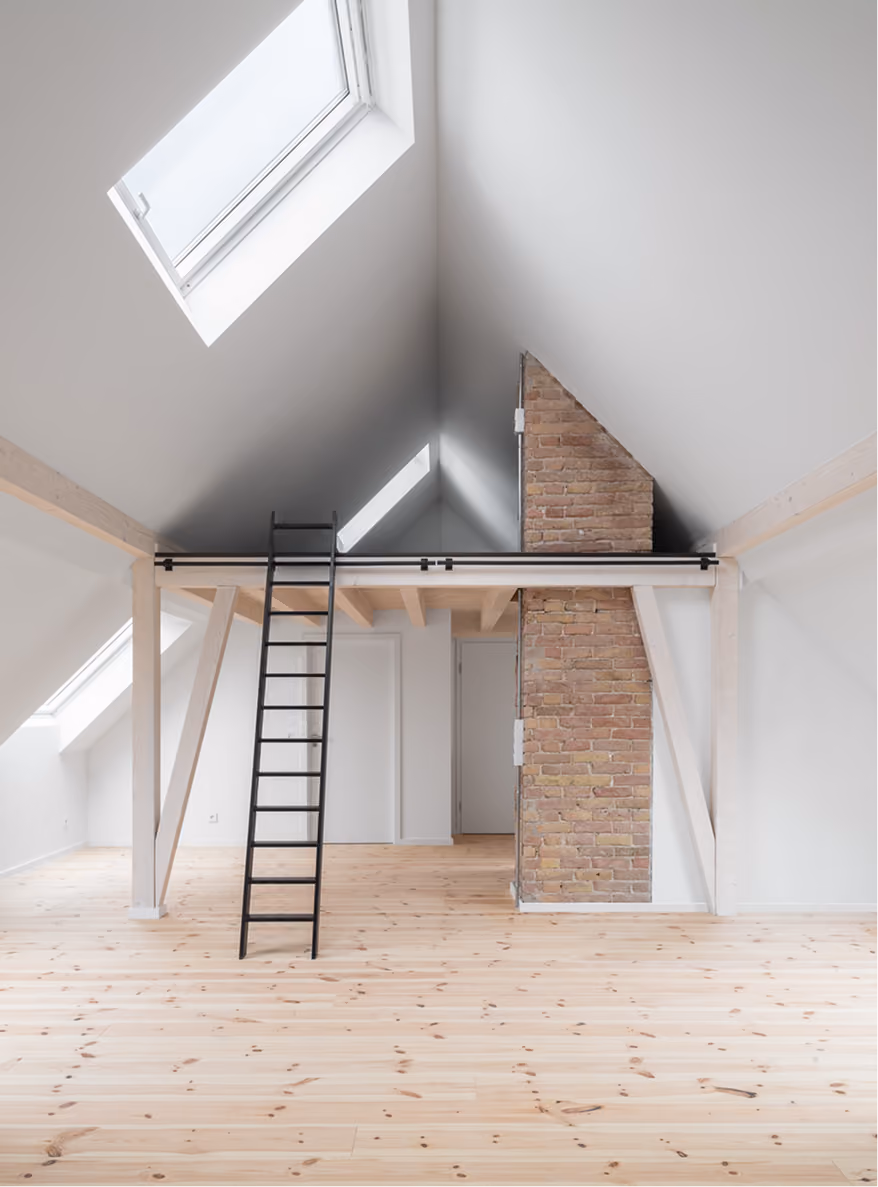Dachraum der Maisonette mit Spitzdach, zwei Holzleitern zu erhöhter Galerieebene mit Backsteinwand, Dachflächenfenster