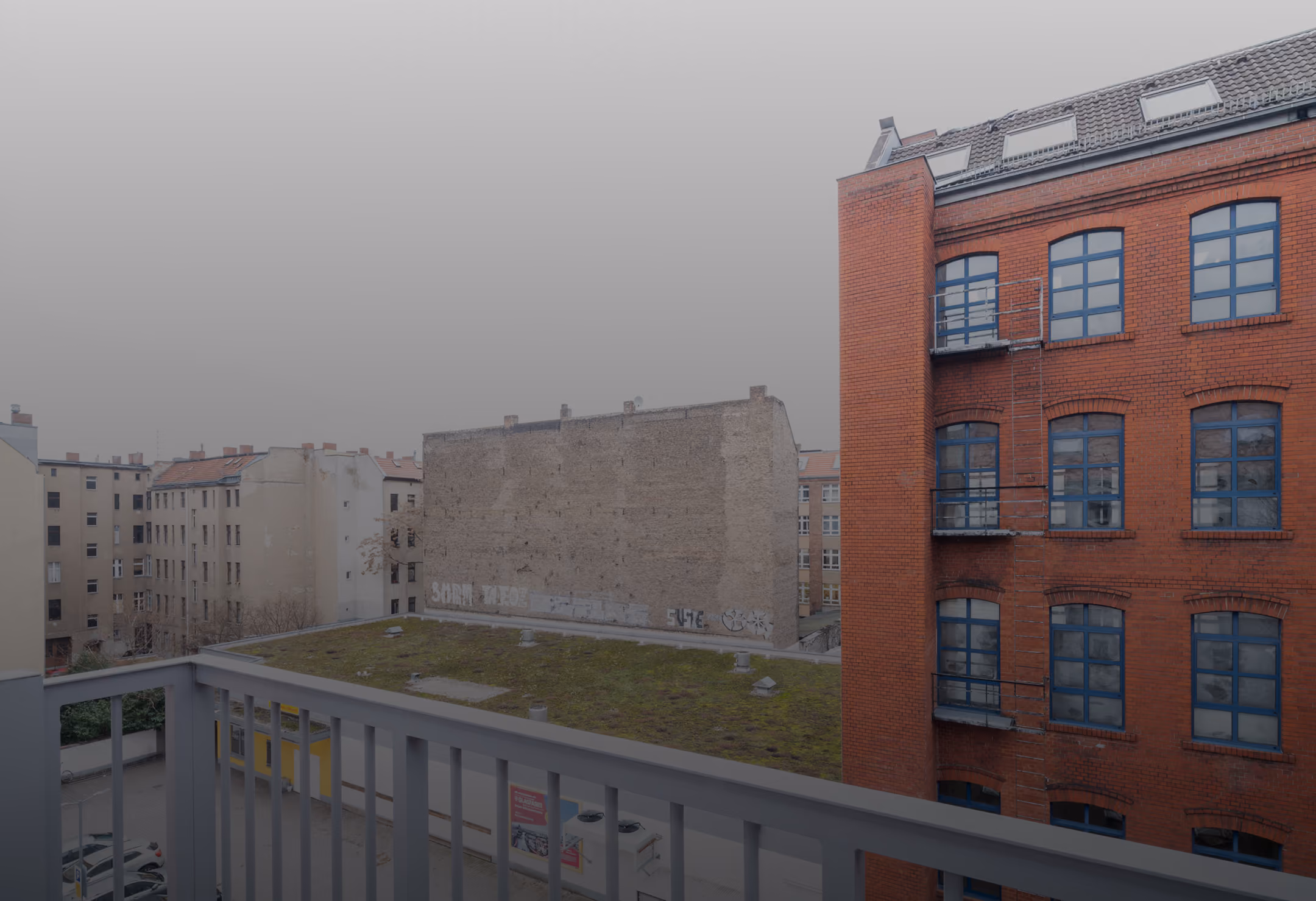 Blick vom Balkon der Maisonette über Berliner Hinterhöfe auf Backstein-Fabrikgebäude im Nebel